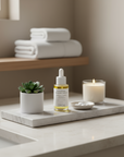 Bottle of SNOA's bakuchiol serum on a marble tray with a candle, plant, and folded towels in the background.